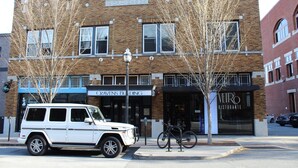 Ein Gebäude mit Ziegelverkleidung, ein weißer SUV davor geparkt, und Geschäfte, darunter das 'Cravens Building' und das 'Viro Ristorante'.