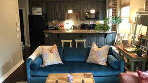 Ein Wohnzimmer mit blauem Sofa, Couchtisch und einer Küche im Hintergrund.