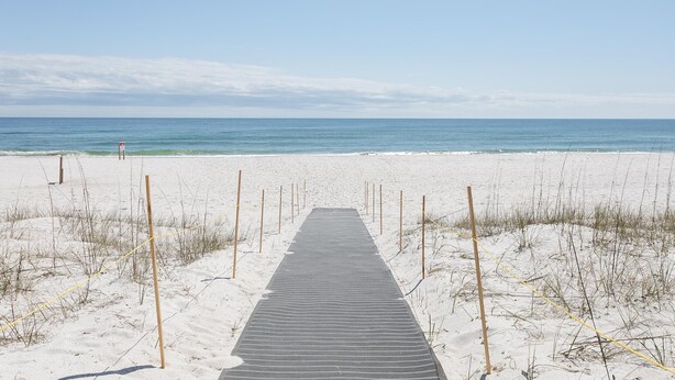 A wooden boardwalk leading to a beach with a clear sky. - Sundown B 23 (Pensacola)
