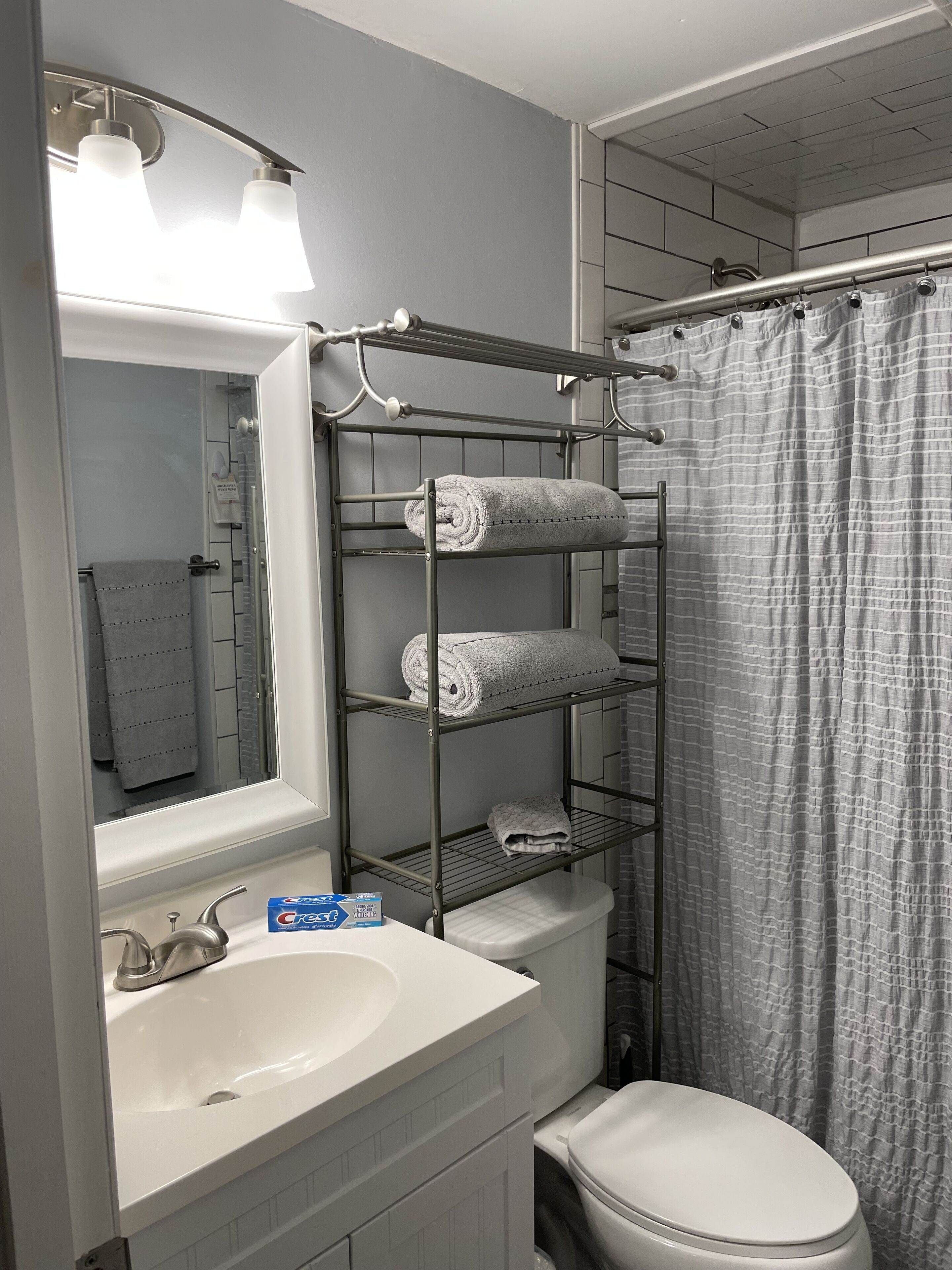 A bathroom with a white sink, a mirror, a towel rack with towels, a shower curtain, and a toilet.