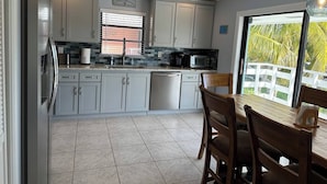 Una cocina moderna con gabinetes grises, un refrigerador de acero inoxidable, un lavavajillas y un comedor con una mesa y sillas de madera.