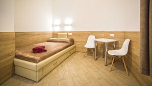 A compact room with a bed, a small table, two chairs, and a wall-mounted light fixture. - Smart Apartment Chornovola 21b (Lviv)
