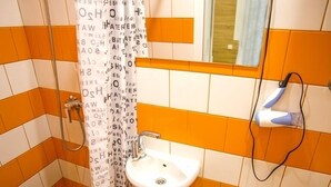 A bathroom with orange and white tiles, a white sink, a toilet, and a shower with a patterned curtain. - Smart Apartment Chornovola 21b (Lviv)