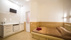 A bedroom with a bed, a bedside table, a TV mounted on the wall, and a door leading to another room. - Smart Apartment Chornovola 21b (Lviv)