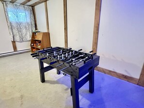 Et bordfodboldbord i et rum med trægulv og et vindue med gardin med et træmotiv.