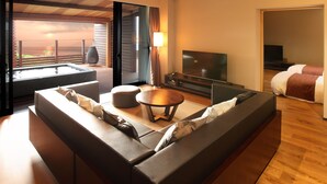 A modern hotel room with a large sofa, a TV, a small table, and a balcony with a view. - Beachside Onsen Resort Umi (Kyonan)