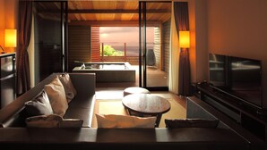 A modern living room with a sofa, a TV, a table, and a balcony with a view. - Beachside Onsen Resort Umi (Kyonan)