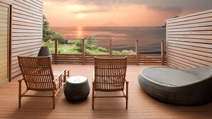 A balcony with two wicker chairs and a round ottoman, overlooking a scenic ocean view with a sunset. - Beachside Onsen Resort Umi (Kyonan)