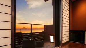A modern interior with a wooden floor, a glass door leading to a balcony with a view of the sunset over the ocean. - Beachside Onsen Resort Umi (Kyonan)