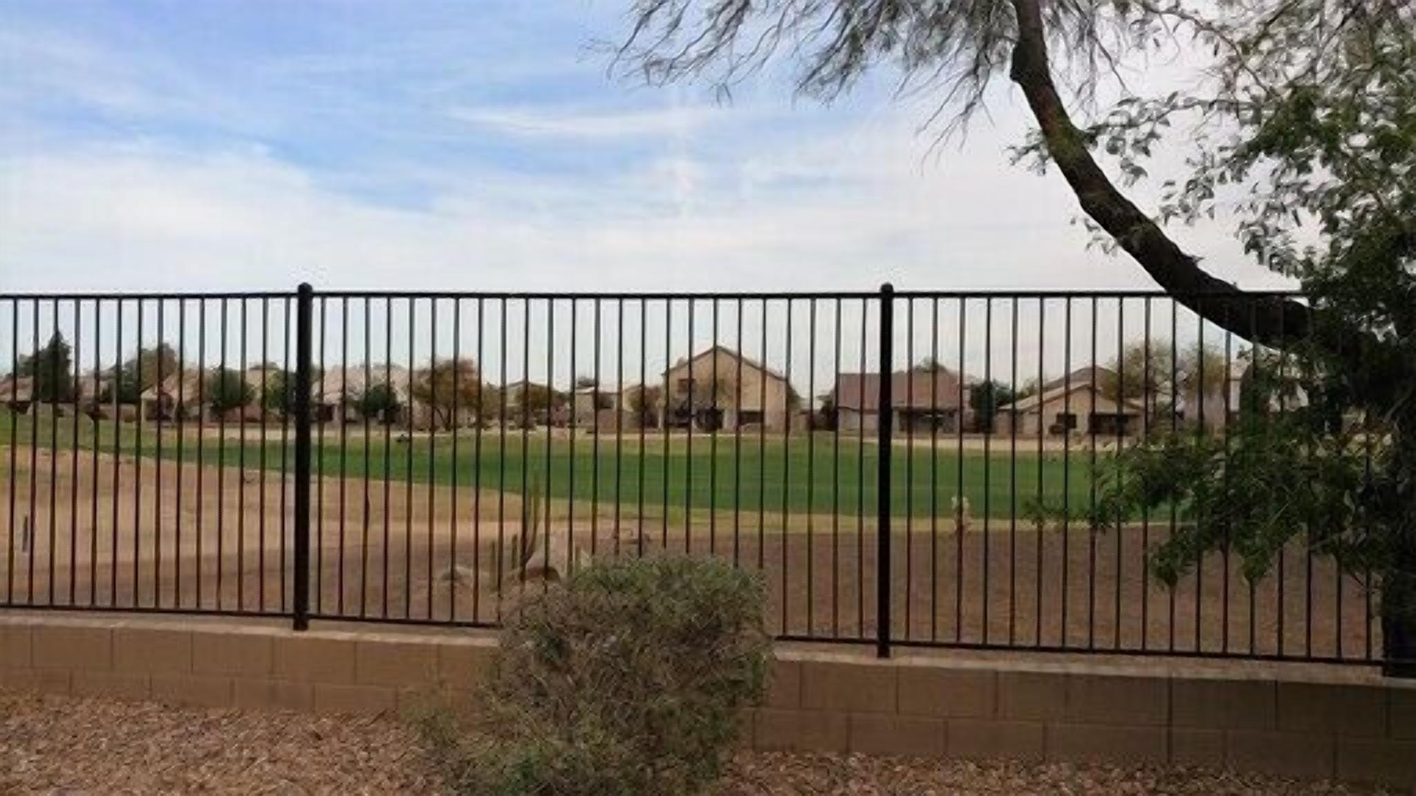 A fenced sports field with a brick wall and a tree in the foreground.