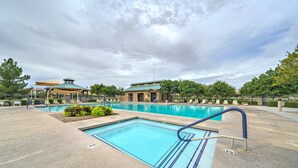 Una piscina amb una zona de solàrium enrajolada, un espai cobert per seure i un edifici amb teulada verda al fons.