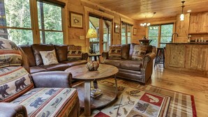 A cozy cabin interior with leather sofas, a wooden coffee table, and a plaid rug.