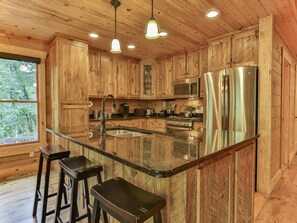 A wooden cabin kitchen with a central island, stainless steel appliances, and a large window. - Southern Grace by Mountain Oasis | Creekfront Trout Fishing Cabin in McCaysville Near Blue Ridge (McCaysville)