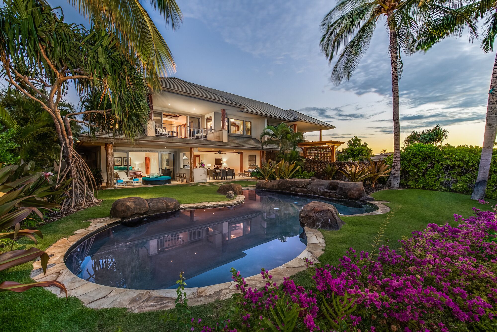 A two-story house with a swimming pool, surrounded by tropical plants and flowers.