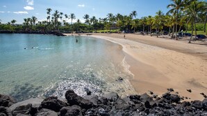 Una playa con agua cristalina, palmeras y una costa rocosa.