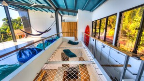 Un hamac suspendu au plafond, une armoire en bois et une planche de surf appuyée contre un mur.