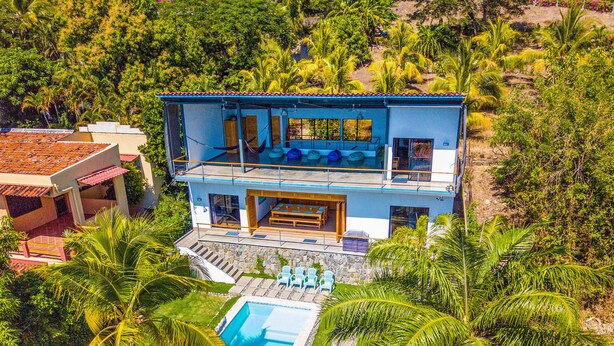 Une maison moderne à deux étages avec une piscine, entourée d’une végétation luxuriante.