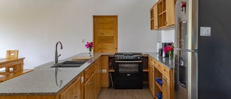 A compact kitchen with wooden cabinets, a built-in oven, a stainless steel refrigerator, and a small dining area with a bench.