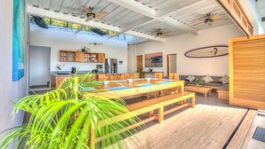 Un vaste espace de vie comprenant un coin repas avec une table en bois, des bancs et, au fond, une cuisine.