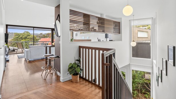A modern kitchen with a view of the outdoors, a dining area with a view, and a staircase leading to a balcony.