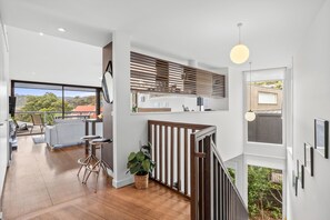 A modern kitchen with a view of the outdoors, a dining area with a view, and a staircase leading to a balcony.