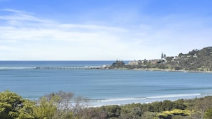 A coastal landscape with a pier extending into the sea, a hill with buildings, and dense greenery in the foreground.