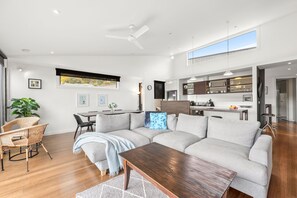 A modern living room with a sectional sofa, a dining table, and a kitchen area with a countertop and cabinets. - Breakers 12 (Lorne)