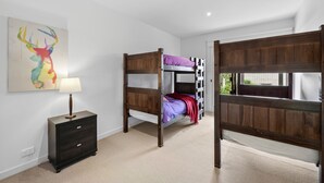 A room with bunk beds, a bedside table with a lamp, and a wall-mounted painting.