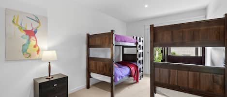 A room with bunk beds, a bedside table with a lamp, and a wall-mounted painting.