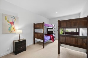A room with bunk beds, a bedside table with a lamp, and a wall-mounted painting. - Breakers 12 (Lorne)