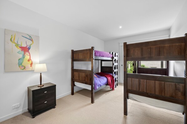 A room with bunk beds, a bedside table with a lamp, and a wall-mounted painting.