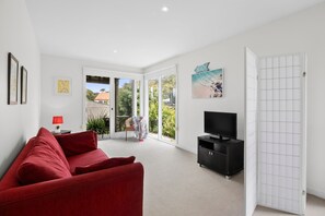 A modern living room with a red sofa, a TV on a black stand, and a door leading to a balcony with a view of the outdoors.