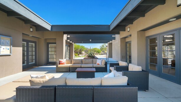 Une terrasse extérieure couverte, aménagée avec un canapé modulable, des meubles en osier et un pot de fleurs.