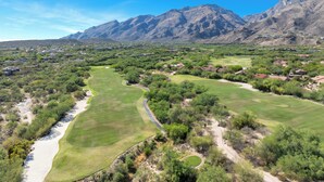 Un parcours de golf doté de plusieurs allées et de nombreux bunkers de sable, entouré d’un paysage désertique et de montagnes.