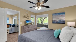Une chambre à coucher avec un lit, un ventilateur de plafond, une commode, une fenêtre donnant sur un beau paysage et un tableau accroché au mur.