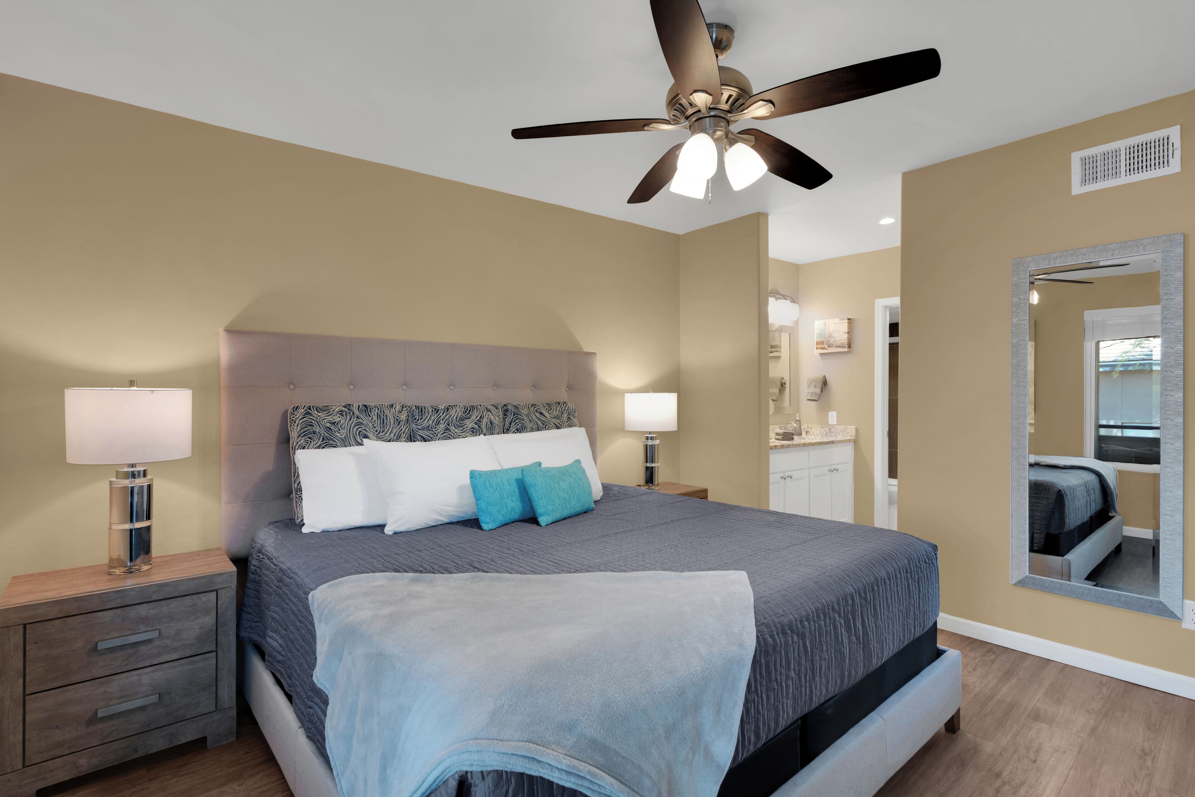 Un dormitorio con cama, mesitas de noche, ventilador de techo y un espejo grande.
