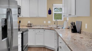 Une cuisine moderne avec des meubles blancs, un réfrigérateur en acier inoxydable, un plan de travail en granit et une fenêtre offrant une belle vue.