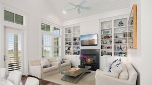 Una sala de estar con muebles blancos, una chimenea y una estantería llena de objetos decorativos.