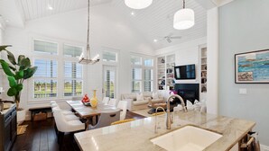 Amplia sala de estar con una isla de cocina grande, muebles blancos y vistas al exterior.