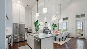 Una cocina moderna con electrodomésticos de acero inoxidable, una isla grande con un fregadero e iluminación colgante.