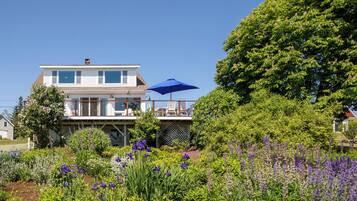 A two-story house with a balcony, surrounded by a garden with various plants and flowers.