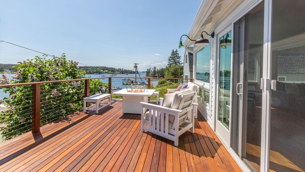 A wooden deck with outdoor furniture, a table, and a view of the water. - Gardenwalk Crest, Elevated Harbor Views, Deck and Village Setting (Port Clyde)