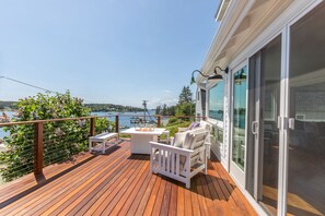 Una terraza de madera con mobiliario exterior, una mesa y vista al agua.