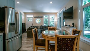 Una cocina moderna con un refrigerador de acero inoxidable, una mesa de comedor con sillas, un sofá y un televisor montado en la pared.