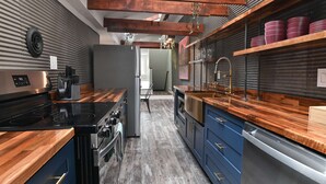 A modern kitchen with a built-in oven, stove, and dishwasher, wooden countertops, and blue cabinets.