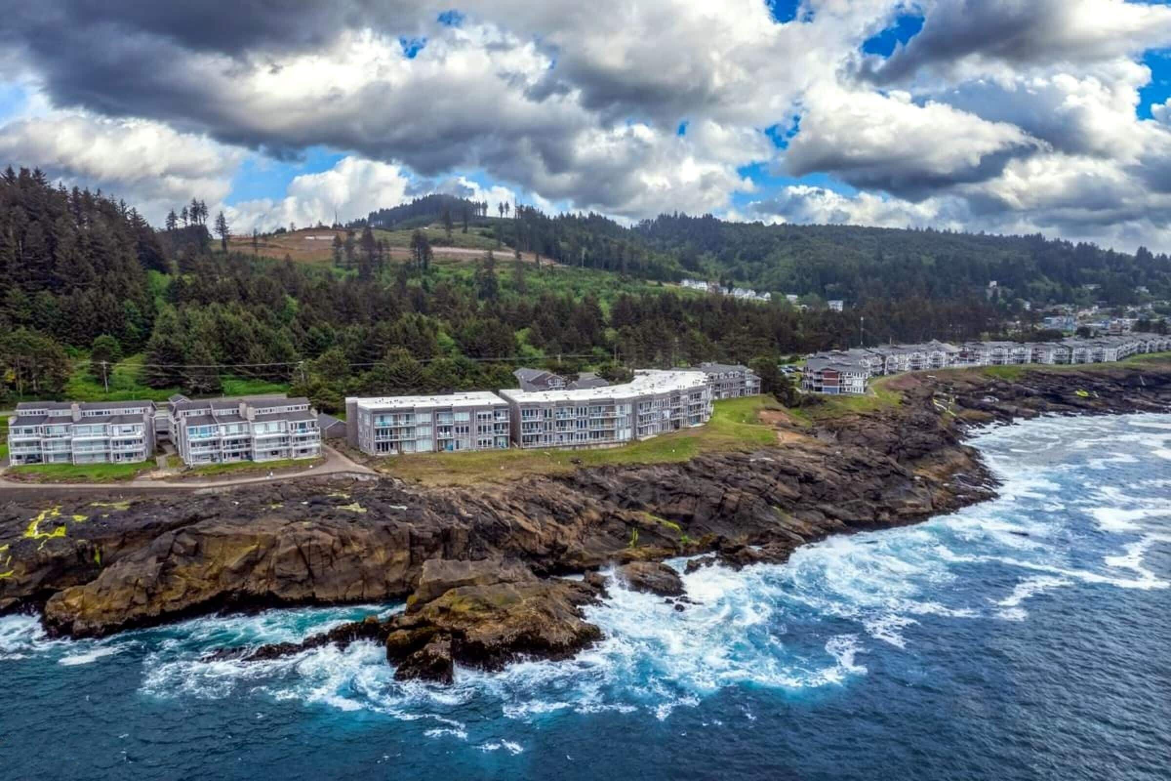 Ein Küstenhotel mit mehreren Gebäuden, einer felsigen Küstenlinie und Blick auf das Meer und die dahinterliegenden Hügel.