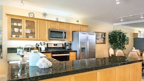 A modern kitchen with wooden cabinets, stainless steel appliances, granite countertops, and a dining area with a large plant. - The Lighthouse, Whale Watching, Fireplace & Pool (Depoe Bay)