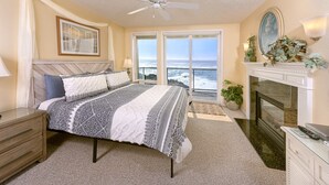A bedroom with a bed, a nightstand, a ceiling fan, a fireplace, and a view of the ocean. - The Lighthouse, Whale Watching, Fireplace & Pool (Depoe Bay)