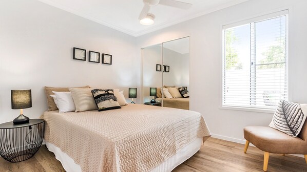A bedroom with a bed, bedside tables, a chair, a large mirror, and a window with blinds. - PEACEFUL PRIVATE WATERFRONT APARTMENT (NOOSAVILLE)