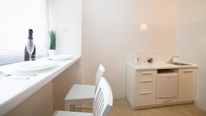 A modern kitchen with white cabinetry, a built-in sink, and a window with blinds. - Smart Apartment Teodora 5a (Lviv)